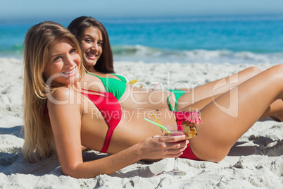 Cheerful tanned blonde and brunette taking sun drinking cocktail
