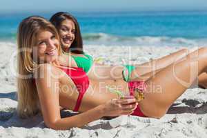 Cheerful tanned blonde and brunette taking sun drinking cocktail