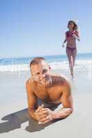 Smiling man lying on the sand while woman running to him