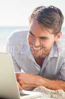 Cheerful handsome man on the beach with his laptop