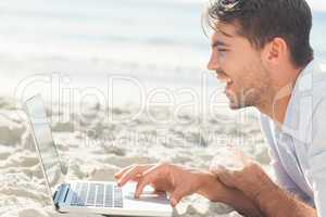 Happy handsome man on the beach using his laptop