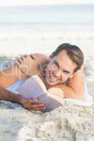 Smiling handsome man on the beach reading a book