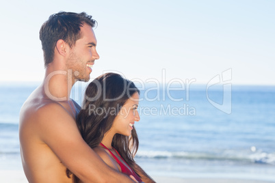 Happy couple in swimsuit hugging while looking at the water
