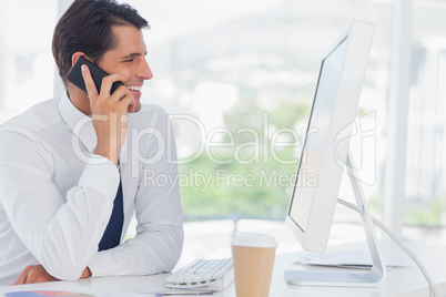 Cheerful businessman on the phone while working on his computer