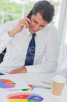 Smiling businessman on the phone analyzing graphs