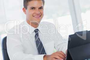 Smiling young businessman working on his tablet pc