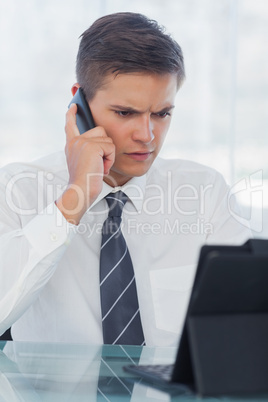 Frowning young businessman working on his tablet pc