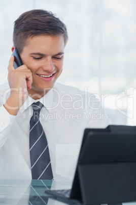 Happy young businessman on the phone while working on his tablet