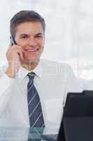 Cheerful young businessman on the phone while working on his tab
