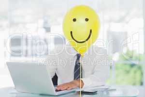 Yellow balloon with happy face hiding businessmans face