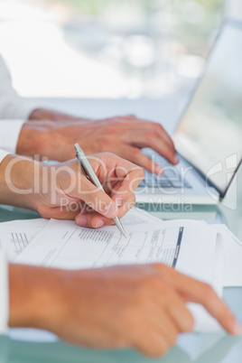Businessman analyzing documents while other working on laptop