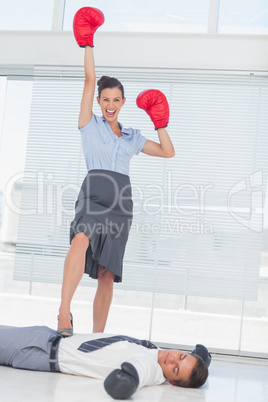 Businesswoman standing on defeated businessman wearing boxing gl