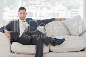 Serious businessman in suit posing sitting on sofa