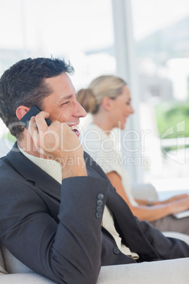 Cheerful businessman on the phone with his colleague working on