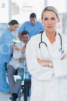 Serious blond doctor posing with colleagues in background
