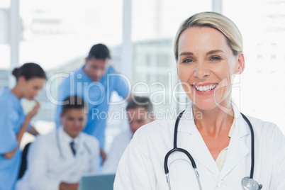 Cheerful blond doctor posing with colleagues in background