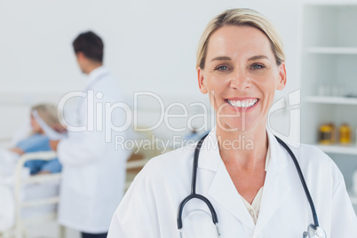 Smiling blond doctor posing with doctor attending patient on bac