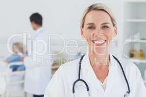 Smiling blond doctor posing with doctor attending patient on bac