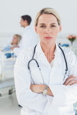 Serious doctor posing with doctor attending patient on backgroun