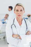 Serious doctor posing with doctor attending patient on backgroun