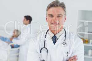 Experienced doctor posing with doctor attending patient on backg