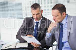 Concentrated businessmen analyzing documents on their tablet