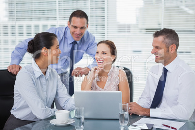 Cheerful colleagues around laptop working together