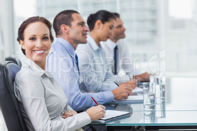 Businesswoman smiling at camera while her colleagues listening t