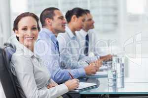 Businesswoman smiling at camera while her colleagues listening t