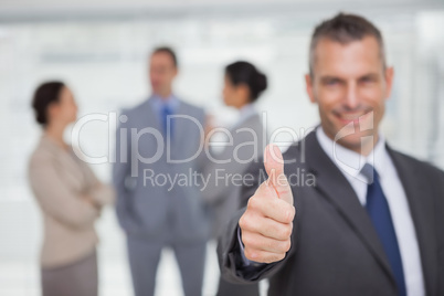 Smiling manager showing thumb up with employees in background