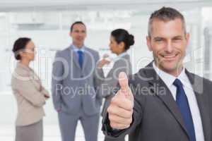 Cheerful manager showing thumb up with employees in background