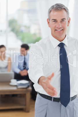 Executive standing on foreground holding out his hand