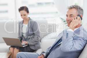 Businessman on the phone while his colleague working on her lapt