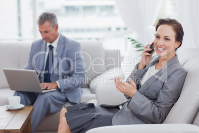 Businesswoman calling while her colleague working on his laptop