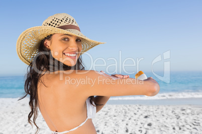 Smiling attractive brunette with straw hat putting on sun cream