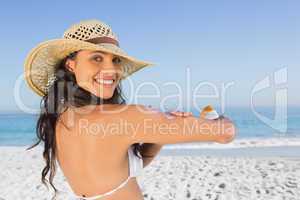 Smiling attractive brunette with straw hat putting on sun cream