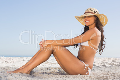 Attractive brunette in white bikini posing while sitting