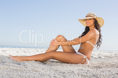 Smiling attractive brunette in white bikini posing while sitting