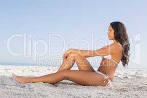 Thoughtful attractive brunette in white bikini posing while sitt
