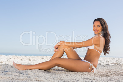 Cheerful attractive brunette in white bikini posing while sittin