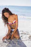 Happy young sexy woman touching sand