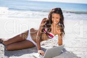 Smiling sexy young woman in bikini using her laptop