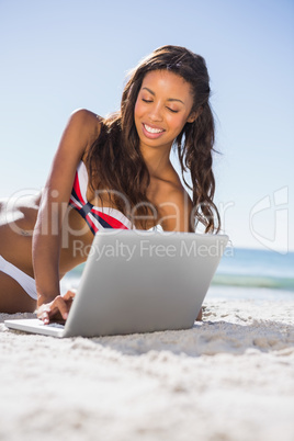 Smiling attractive young woman in bikini with her laptop