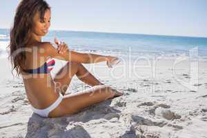 Attractive woman in bikini applying sun cream on her shoulder