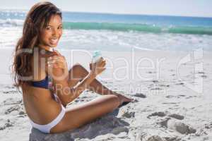 Smiling woman in bikini applying sun cream on her shoulder