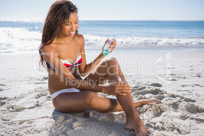 Smiling woman in bikini applying sun cream on her leg