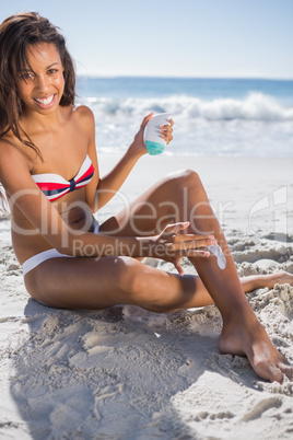 Smiling woman applying sun cream on her leg