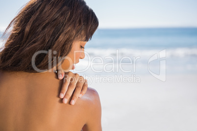 Pensive woman applying sun cream on her shoulder