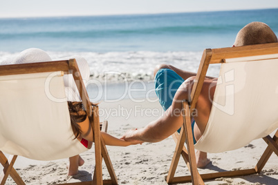 Cute couple holding hands while lying on their deck chairs