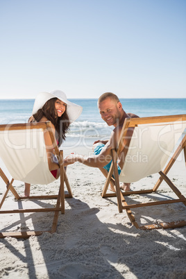 Cute couple smiling at camera while lying on their deck chairs